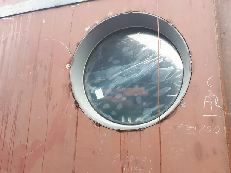 Detailopname van een van onze grote lasbare stalen patrijspoorten gemonteerd op een onbewerkte scheepsromp in aanbouw