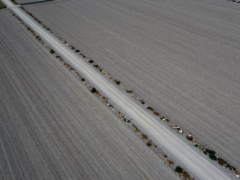 High-altitude aerial drone photograph of a raw land parcel with clear gravel access roads, sharp boundary lines, overcast daylight, desaturated tones, 35mm.