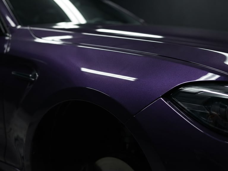Sleek automotive photography of a freshly painted deep purple car fender reflecting soft studio light, high-contrast specular highlights, 50mm lens