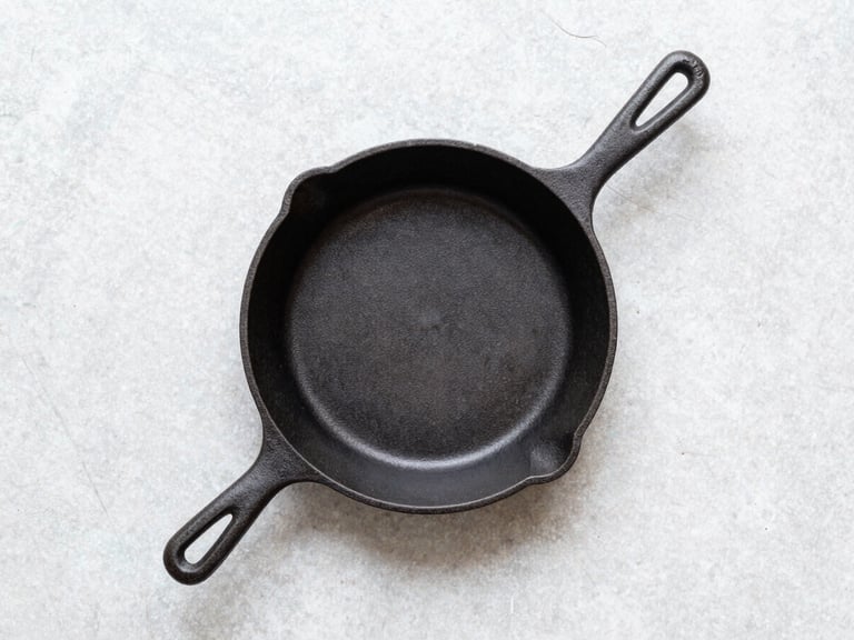 Stark top-down flat lay of a single cast iron skillet on a light grey stone surface, bright natural diffused daylight, sharp focus, 50mm lens