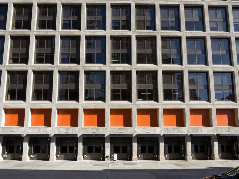 Wide-angle architectural lens view of the Rossi Group Denver headquarters exterior, showing active loading bays and structured concrete design under high-contrast daylight
