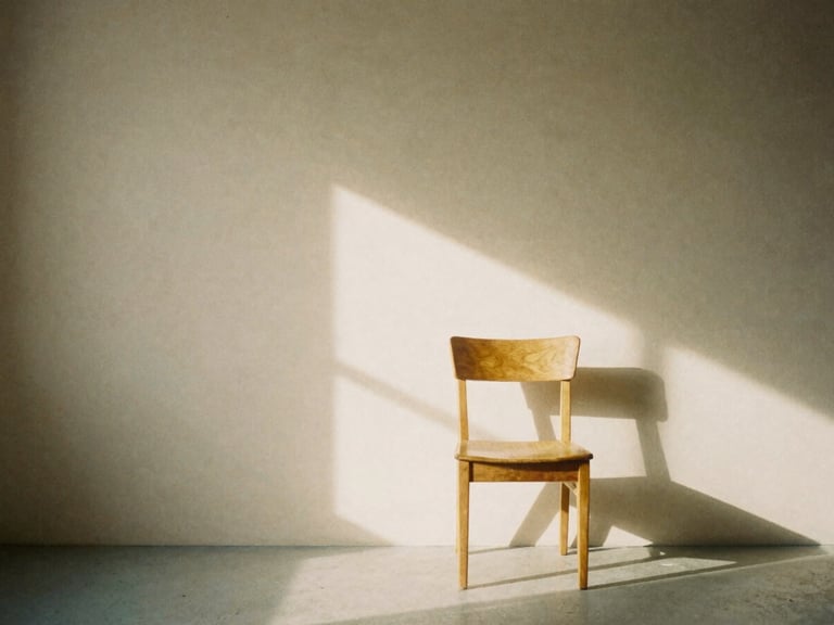 A minimalist photography studio interior with soft natural window light casting gentle shadows on a neutral warm-sand wall, a single oak chair, 35mm film aesthetic.