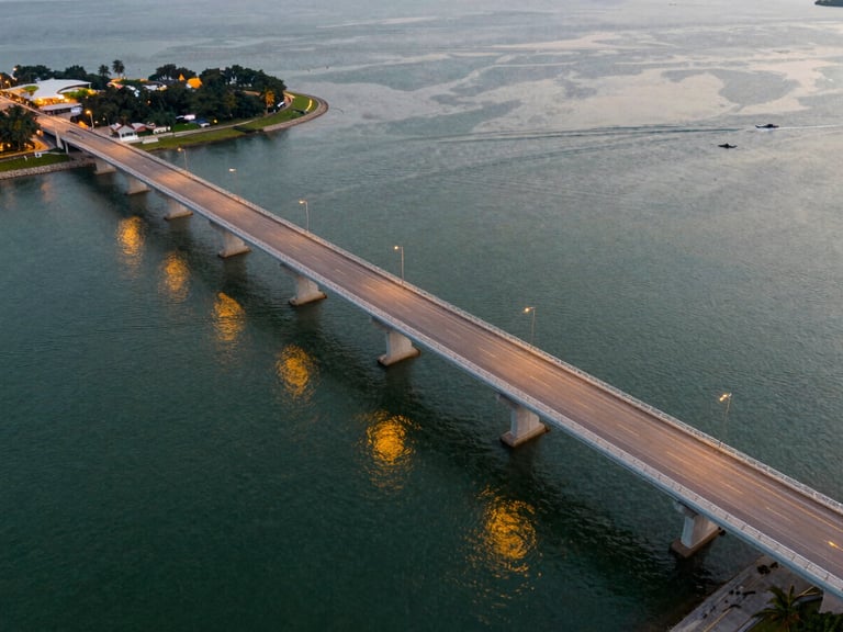 Aerial view of the Singapore-Johor causeway at dusk, golden lights reflecting on the water, clean architectural lines, warm evening light