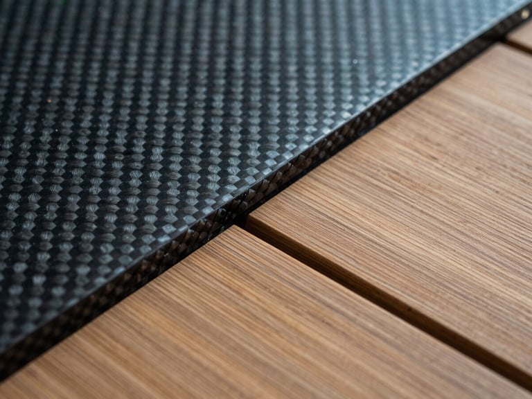 Close-up of raw marine materials including brushed teak decking meeting a carbon fiber weave panel under cool-toned technical lighting