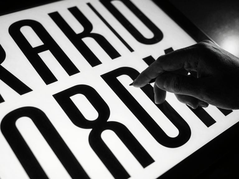 Close-up of a designer's hand manipulating a bold, sans-serif typography layout on a screen, dramatic shadows, high-contrast studio light. High-contrast black and white photography, sharp focus, 35mm film grain.