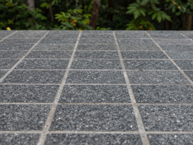 Close-up of perfectly aligned dark granite paving stones with clean grey joints under soft overcast daylight, shallow depth of field, 35mm