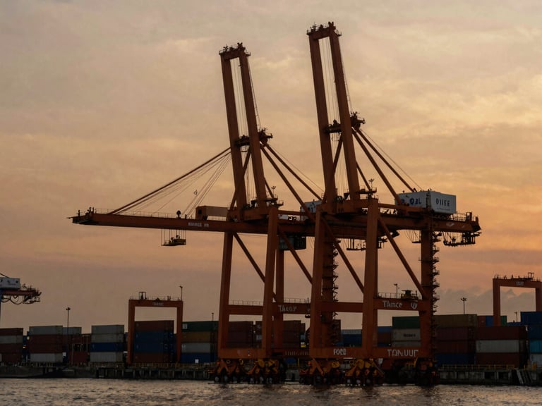 Wide panoramic shot of Tanjung Priok container terminal at dawn, massive orange gantry cranes silhouette against a warm amber sky, high contrast industrial photography