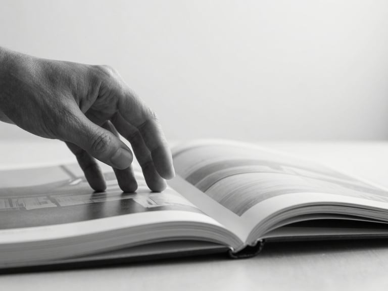 A close-up of a hand gently turning the page of a high-quality art book, soft natural diffused light, desaturated black and white, sharp focus, 35mm architectural lens.