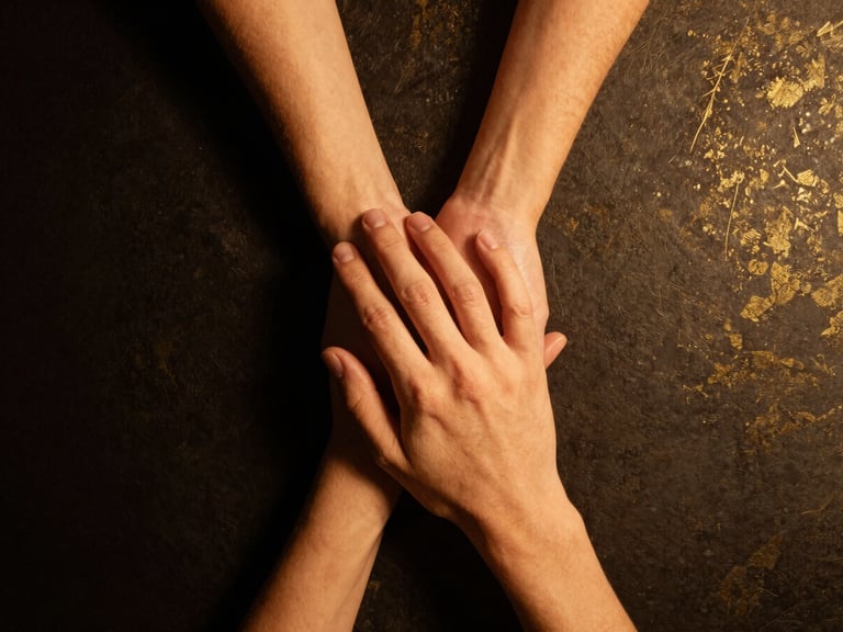 Two hands gently clasped on a dark surface, subtle gold leaf texture in the background, warm golden light, deep black and gold tones, soft shadows, 35mm lens.