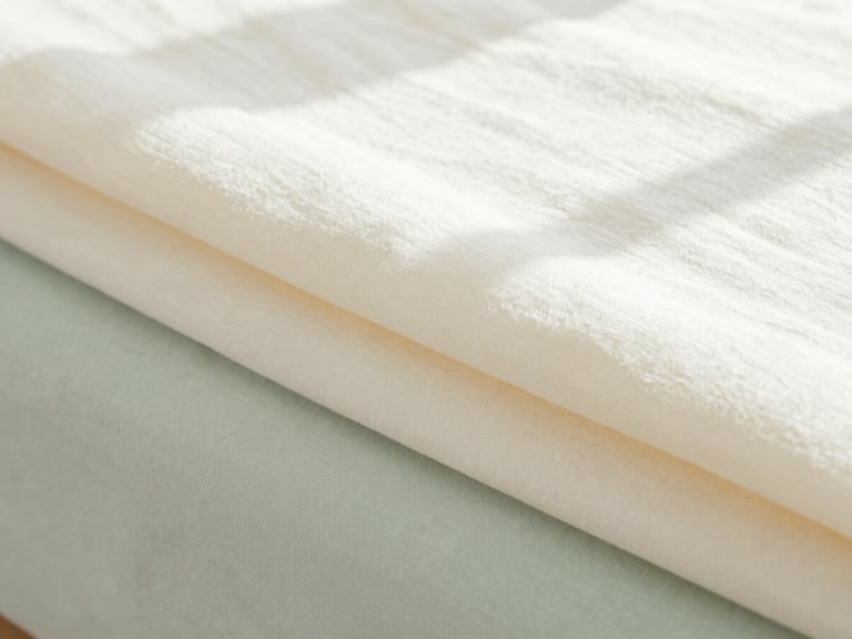 Close up texture of folded cream-colored organic cotton sheets, soft morning sun, minimalist aesthetic