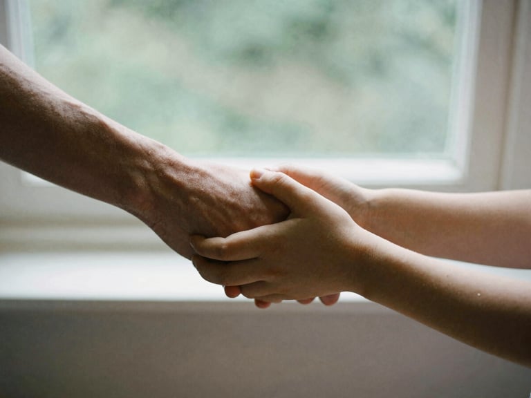 A close-up of two hands, one adult and one child, holding hands gently, soft focus, natural window light, stone tones.