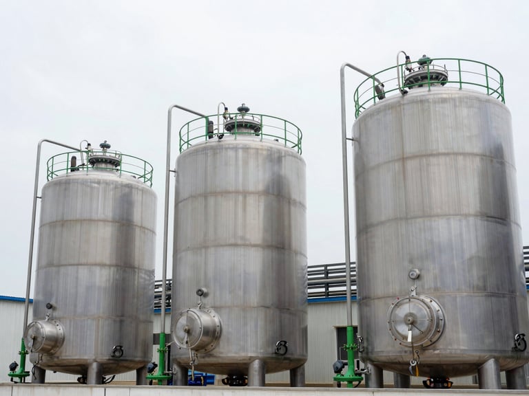 Wide environmental photography of modern chemical reactors and stainless steel storage tanks under clean, bright overcast sky, sharp focus, clinical precision