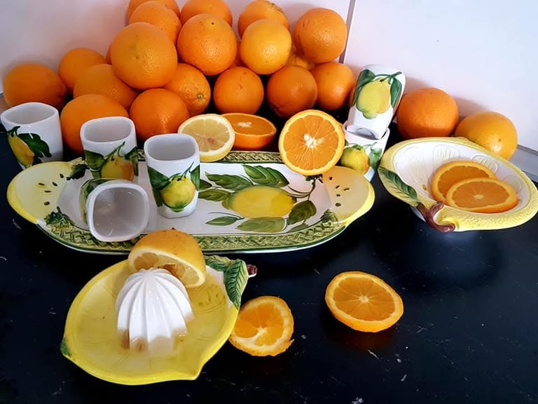 Fresh oranges and lemons arranged with ceramic citrus-themed serving dishes and a manual juicer.