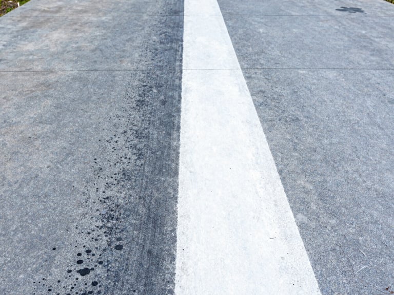High-contrast split shot of a dirty concrete driveway being cleaned, showing a bright white restored path next to dark gray grime, sharp focus