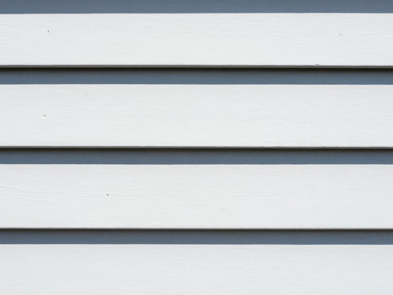 Tight macro shot of clean white vinyl siding next to weathered siding, bright midday sunlight, high contrast