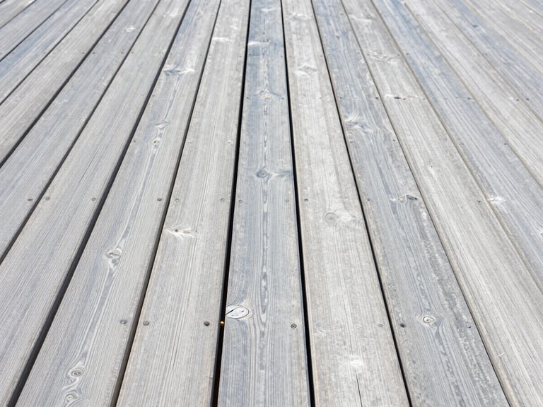 A clean wooden deck with pristine grain next to grey weathered wood, bright midday sun, crisp focus
