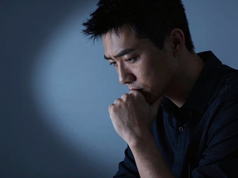 Minimalist studio photography, close-up of a creative professional looking down in deep thought, dramatic lighting, cool blue shadows, sharp focus.