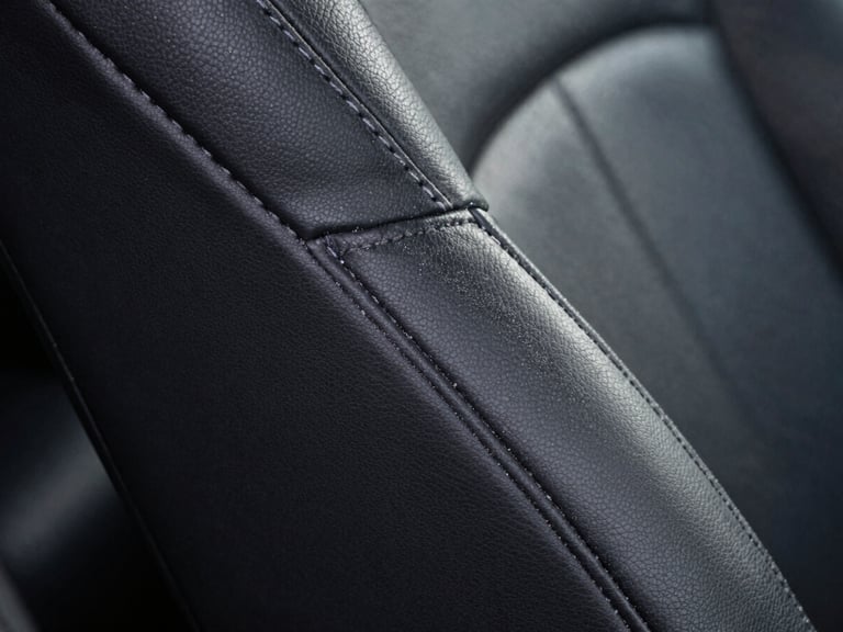 Macro shot of restored black leather grain on a car seat, dust-free stitching, illuminated by clinical white LED light, zero dust particles.