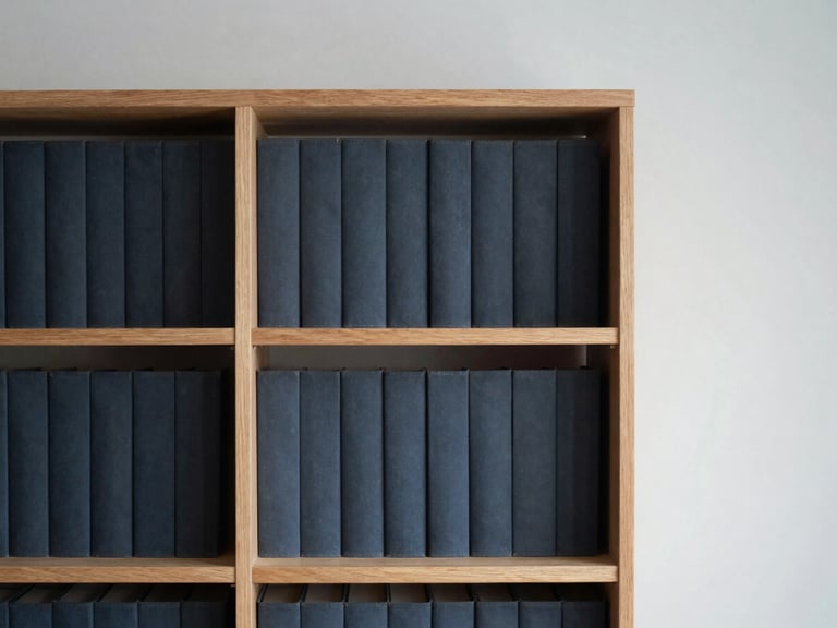 Plano medio de estanterías de madera con tomos académicos encuadernados en tonos oscuros, iluminación lateral suave, enfoque selectivo.