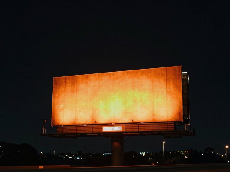 Wide environmental night shot of a colossal highway billboard glowing with vibrant orange light against a deep dark sky, cinematic atmosphere