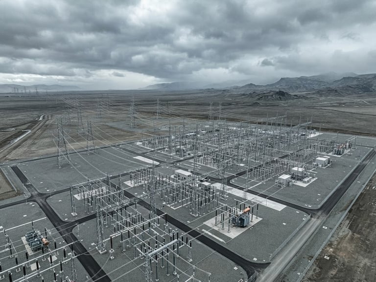 High-voltage substation and transmission lines stretching across a vast flat graded land parcel under a dramatic overcast sky, industrial scale, cool desaturated tones