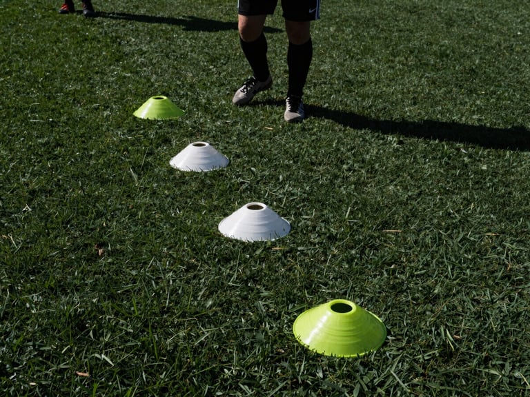 Wide panoramic shot, low angle on a player's feet executing a rapid cone drill on turf, high-contrast natural midday sun, harsh shadows.