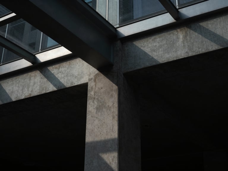 Clean architectural detail of a concrete column meeting a glass ceiling, sharp geometric shadows, dramatic low-key directional light, 35mm lens.