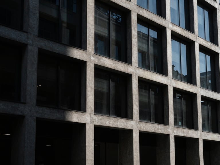 Wide architectural perspective of a concrete and glass building facade, dramatic directional light, cool shadows, dark editorial style