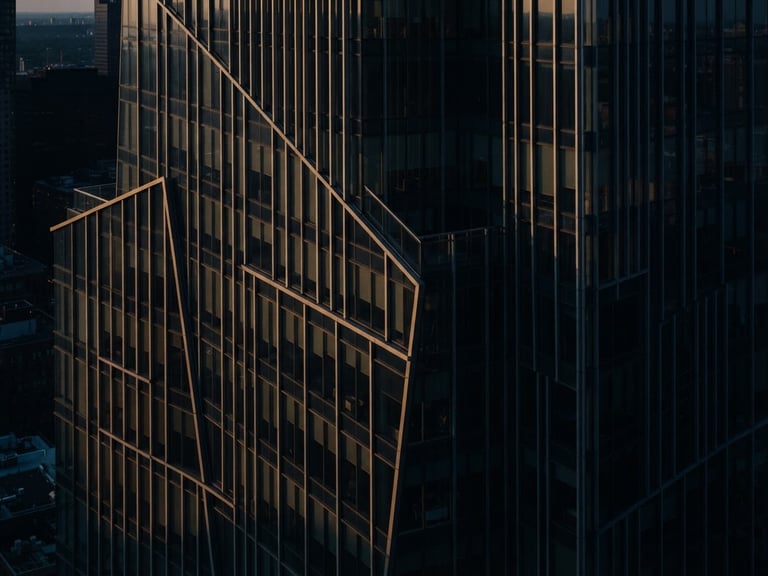 Moody corporate photography of abstract architectural lines of a modern building facade, soft directional window light with deep shadows, deep navy and warm gold tones, 35mm