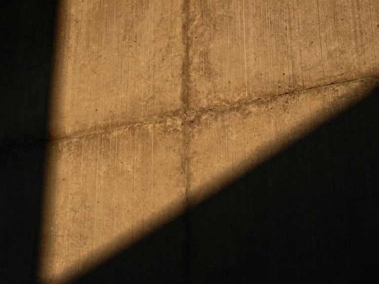 Low-angle shot of a textured concrete wall grazed by warm amber light, casting deep dramatic shadows in the crevices.