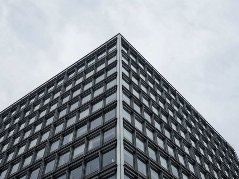 Low-angle architectural crop of a structured steel and glass building corner against a stark overcast sky.