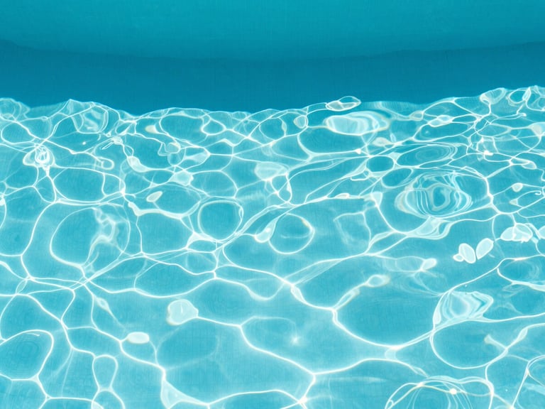 Minimalist overhead shot of crystal clear turquoise pool water with soft natural midday sun reflections and sharp architectural shadows, 35mm, crisp royal blue and white tones