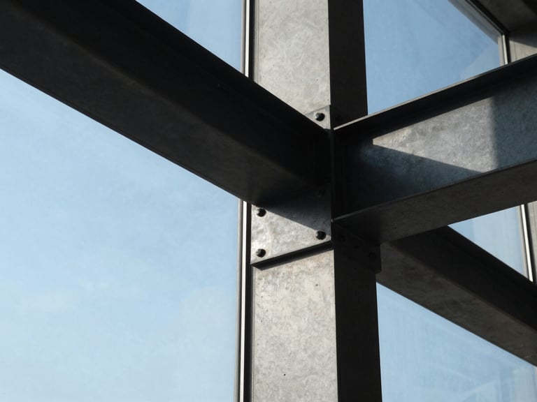 Ultra-tight crop of a structural concrete joint and blackened steel beam intersecting a massive glass pane, natural high-contrast morning light.