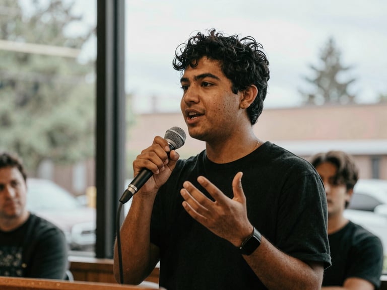 Candid medium shot of a young Seattle advocate speaking passionately into a microphone at a neighborhood forum, natural overcast daylight filtering through window, expressive hand gestures