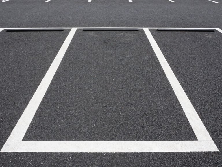 Straight-on eye-level shot of a clean, well-lit urban monthly parking lot in Tokyo, clear white line markings on dark asphalt, bright daylight with high visibility.