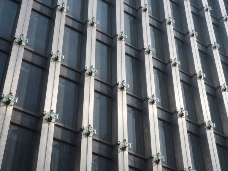 Low-angle architectural shot of heavy-duty glass spider connectors and stainless steel columns on a high-rise building facade, cool daylight, sharp shadows