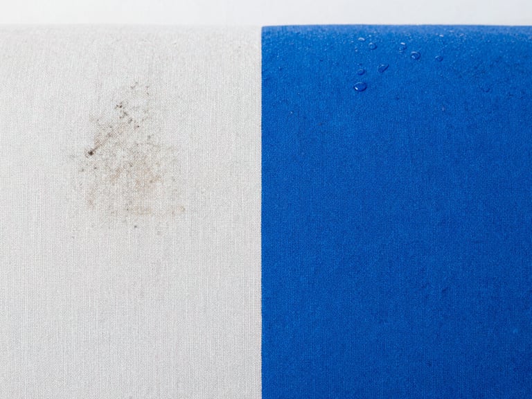 Macro photography of a fabric sofa surface showing a sharp vertical line of clean contrast: the left side is dusty and stained, the right side is pristine and bright blue, water droplets visible, sharp focus.