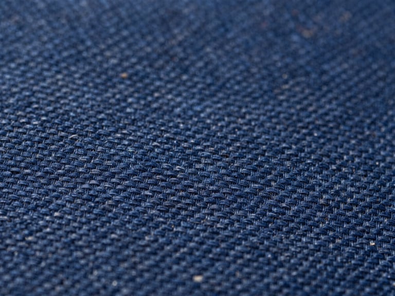 Macro close-up of deep indigo woven fabric showing the precise interlacing of warp and weft threads under bright daylight.