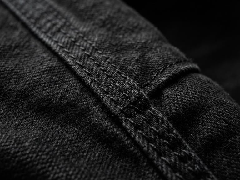 Extreme close-up of a heavy-weight cotton garment seam, structured black fabric texture, sharp directional studio lighting, deep shadows, 35mm lens