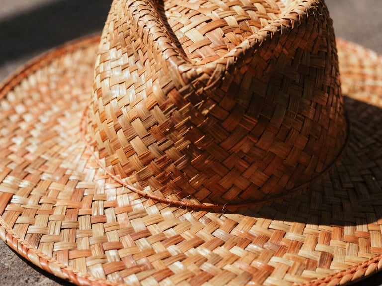 Close-up of a hand-woven palm hat, intricate weave visible, harsh natural sunlight casting deep shadows, warm editorial photography, rich terracotta tones, 35mm film