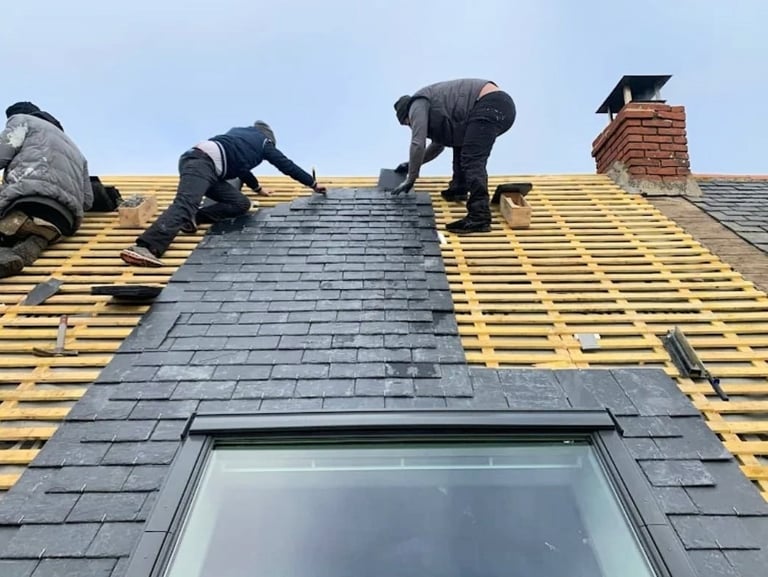 Trois couvreurs posant des ardoises sur charpente de toiture avec Velux