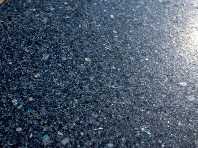 Macro close-up of Crystal Blue granite slab surface in natural daylight — deep charcoal-blue ground with iridescent mineral flecks catching light, polished finish, raking light from upper right revealing surface texture and crystal shimmer