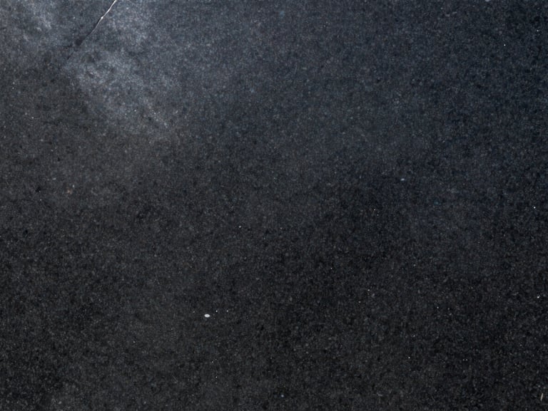 Close-up of Absolute Black granite slab under raking natural daylight — uniform dense black ground with zero visible grain variation, mirror-polished finish, sharp specular highlight running across the upper left of the surface