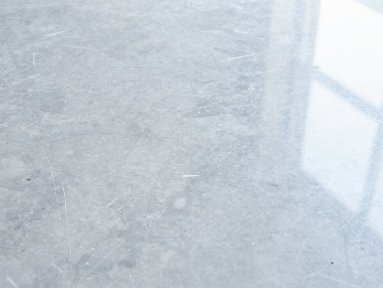 Close-up shot of a heavily scuffed and dull grey marble floor, visible scratches and water stains under soft overhead light