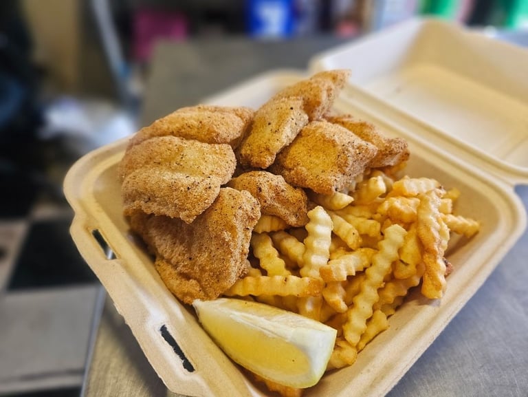 Golden fried catfish and crinkle cut fries with a lemon wedge in a to-go container at Captain's Galley