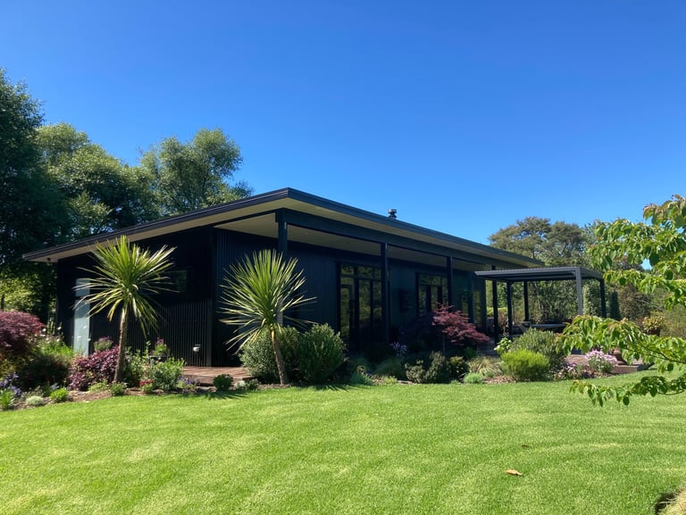 Modern black metal tiny home with a flat roof nestled in a lush green garden with palm trees.