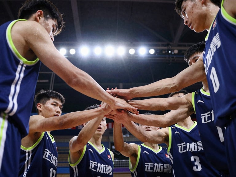 Candid team huddle of youth basketball players placing their hands together, high-contrast stadium lighting, deep blue jerseys, action freeze-frame.