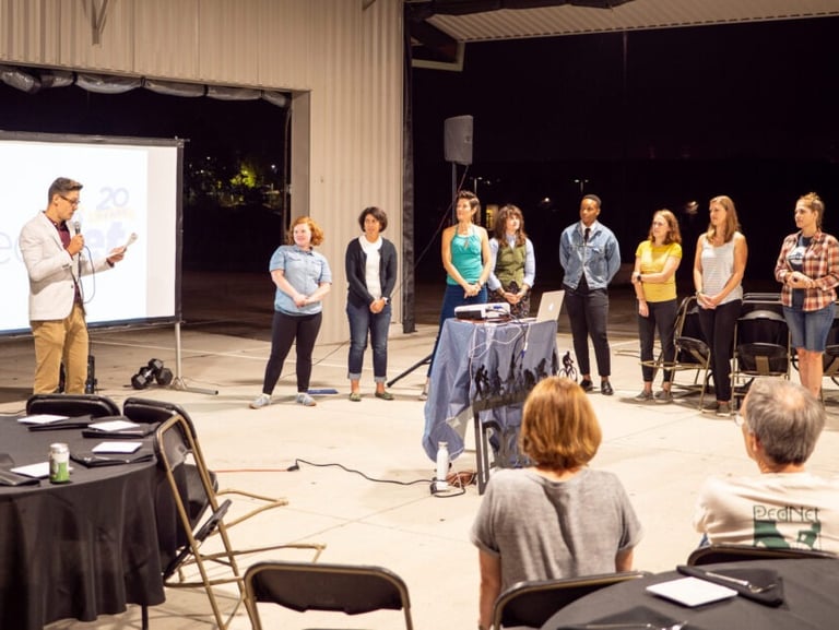 CEO presenting by a screen holding a microphone, with the staff lined up nearby
