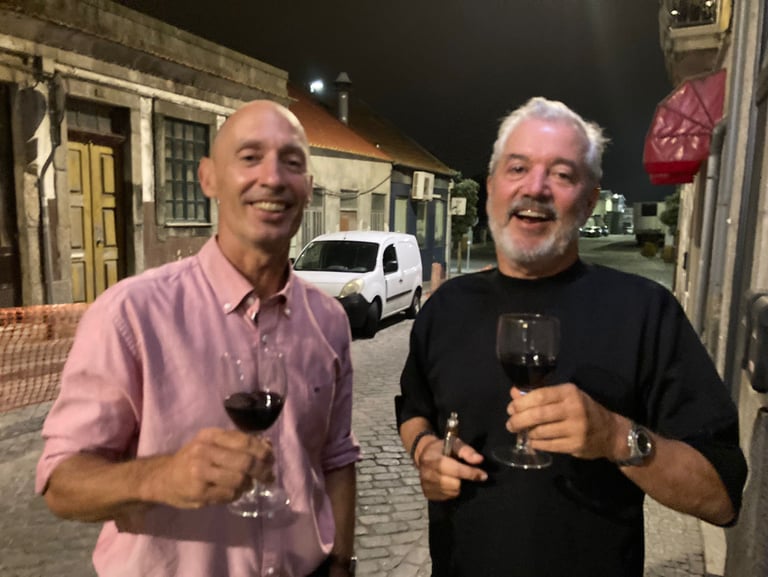 two men standing next to each other holding wine glasses