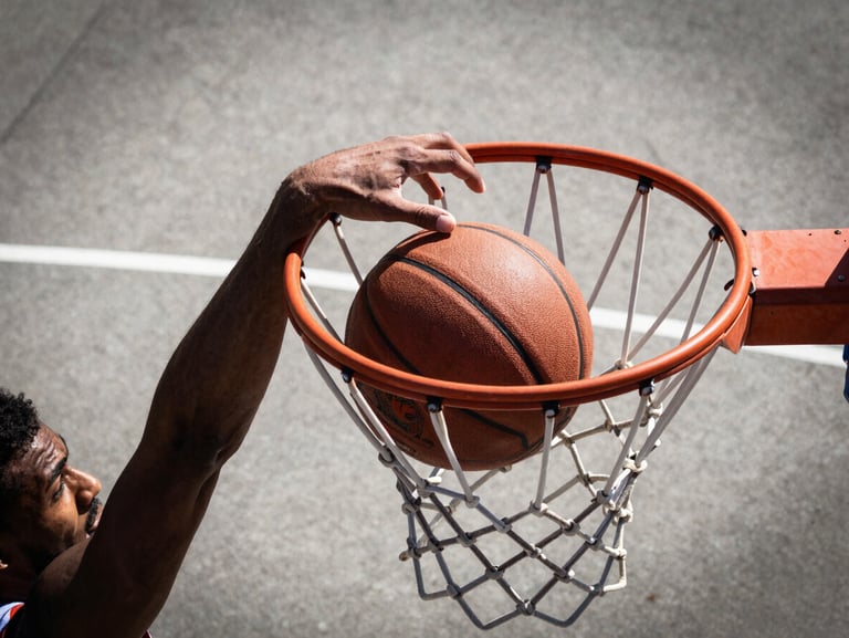 Close-up of a basketball player's hand slamming the ball into the hoop, outdoor concrete court, dramatic high contrast daylight, sharp focus